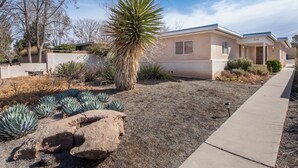 A single-story house with a beige exterior, a front yard with a palm tree, agave plants, and a rock. - Cozy 2bd 2ba near Nob Hill home Garage Parking (Albuquerque)