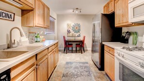 A modern kitchen with wooden cabinets, a stainless steel refrigerator, a gas stove, and a dining area with a table and chairs. - Cozy 2bd 2ba near Nob Hill home Garage Parking (Albuquerque)