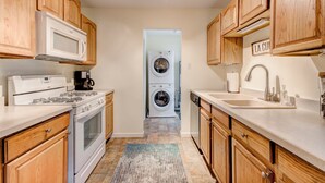 A compact kitchen with wooden cabinets, a stove, microwave, and a double washer-dryer unit. - Cozy 2bd 2ba near Nob Hill home Garage Parking (Albuquerque)