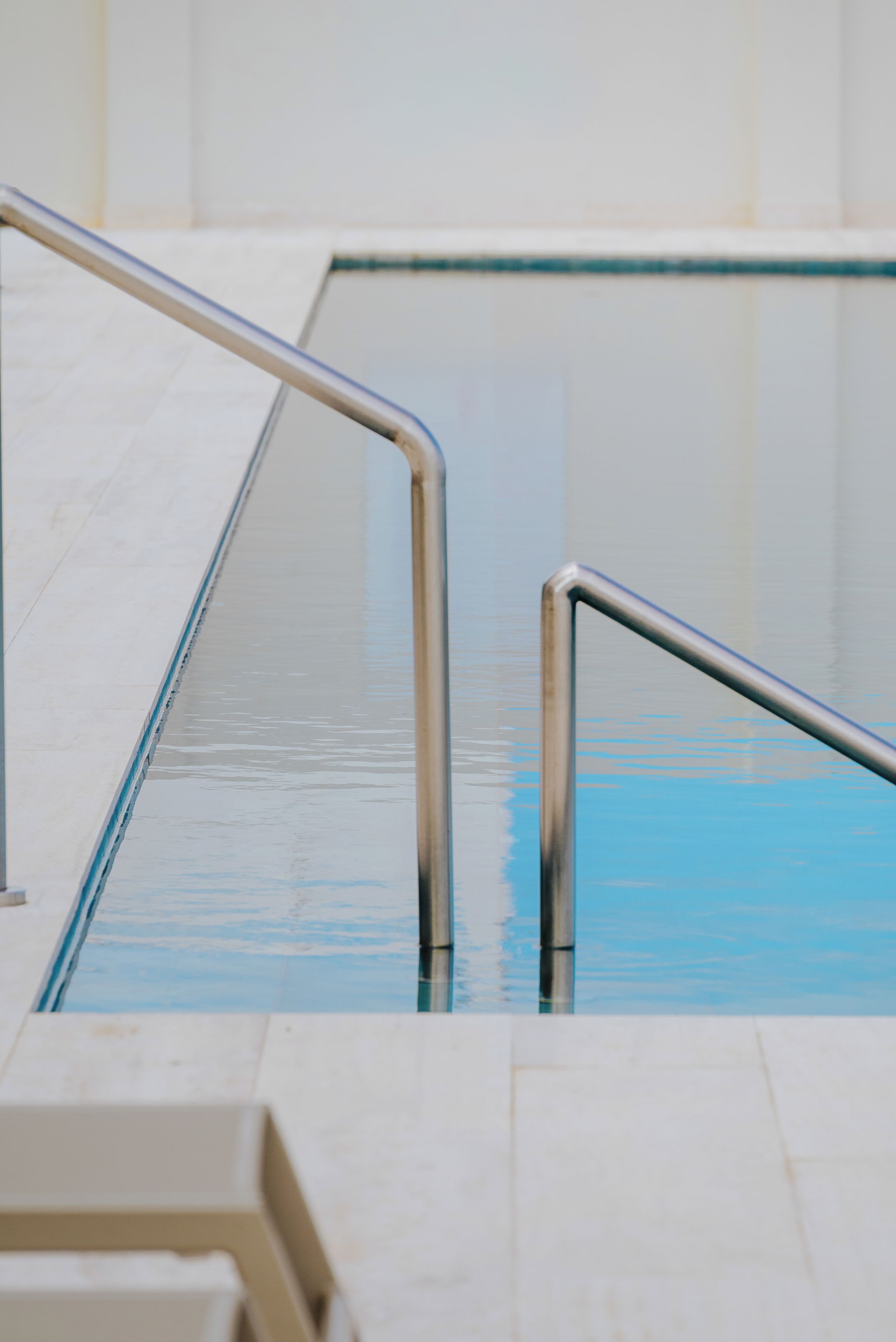 Una piscina con barandillas metálicas y un suelo de baldosas.
