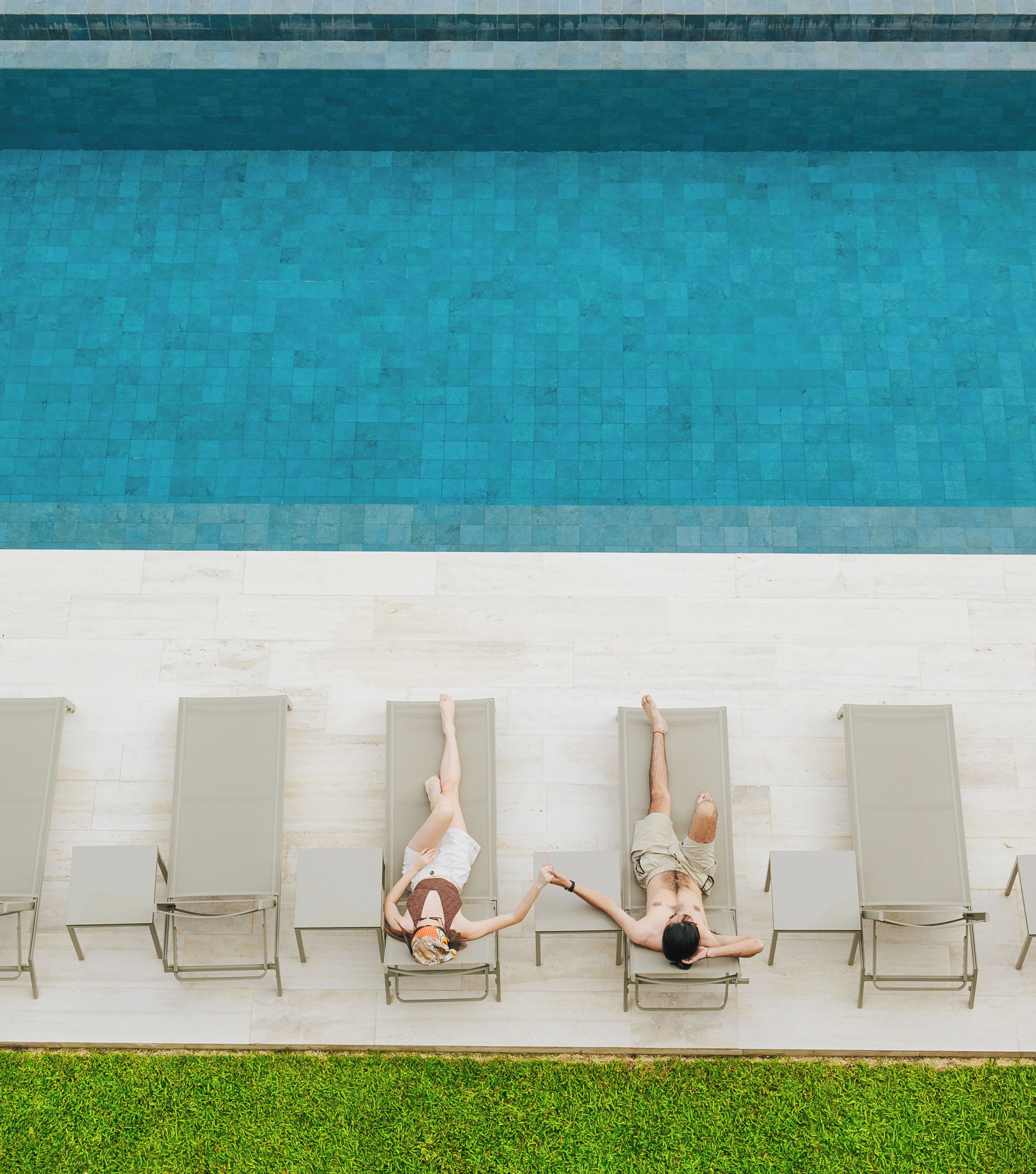 Un área de piscina en la azotea con cuatro sillones de descanso alineados a lo largo del borde, con vista a una piscina.