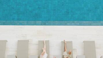Un área de piscina en la azotea con cuatro sillones de descanso alineados a lo largo del borde, con vista a una piscina.