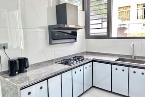 A modern kitchen with a gas stove, black coffee makers, and white cabinets. - Bishui Xincun Yuese Villa (Guangzhou)