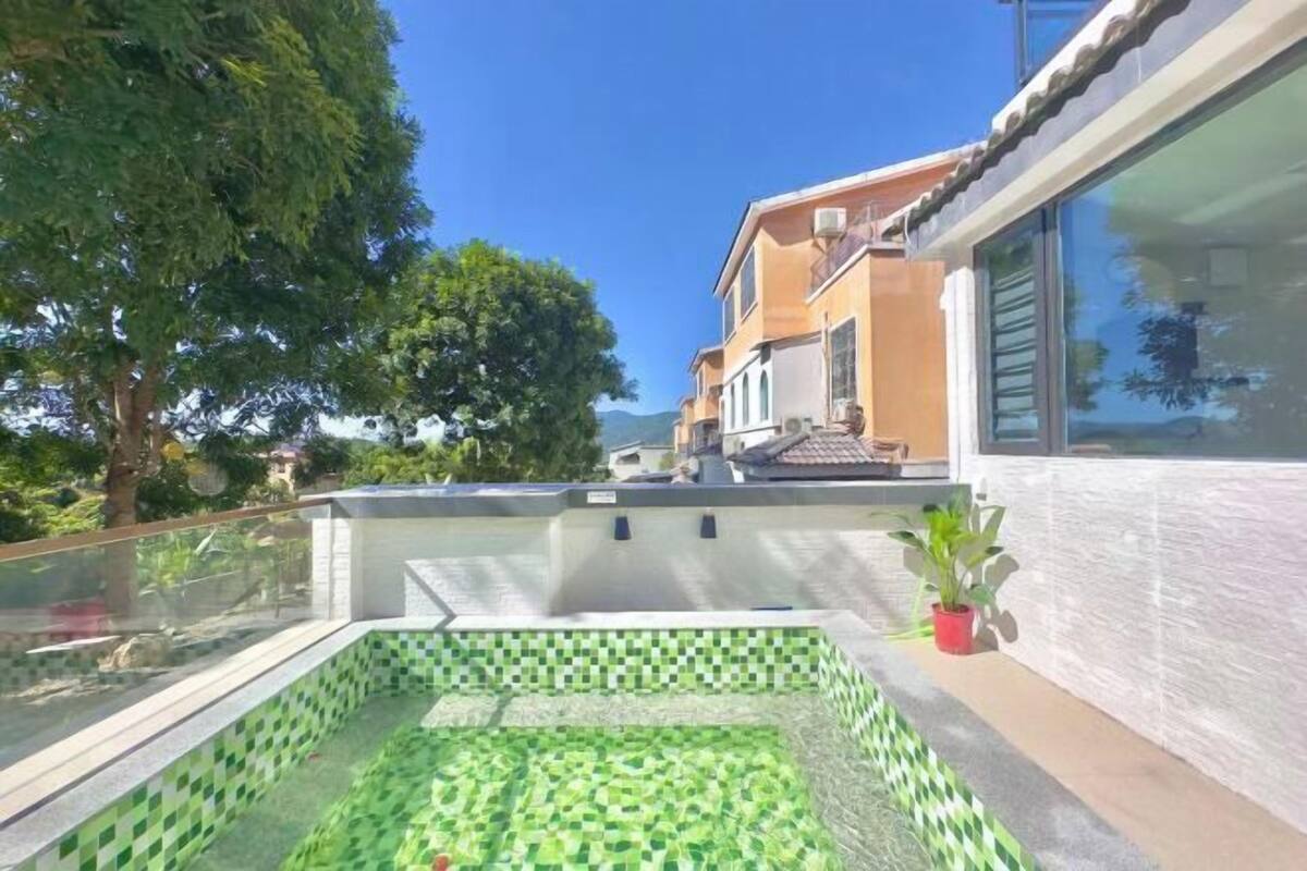A rooftop swimming pool with checkered tiles, surrounded by a glass railing, and adjacent to a building with a tiled exterior.
