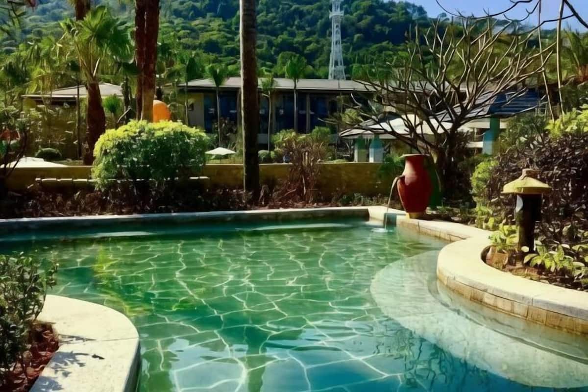 A pool with clear water, surrounded by greenery and a building in the background.