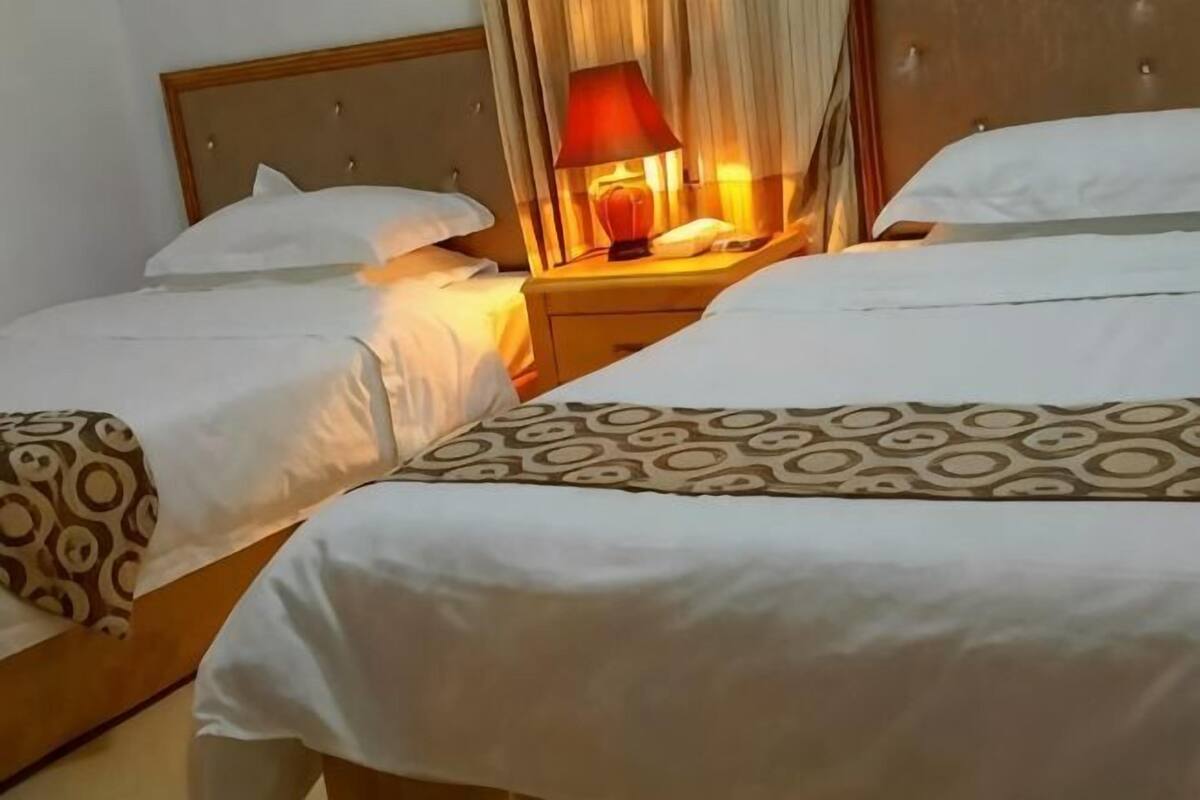 A hotel room with two beds, a bedside table with a lamp, and a headboard.