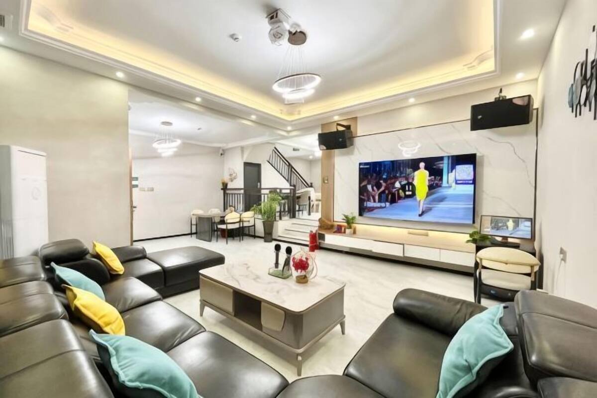 A modern living room with a large flat-screen TV, leather sofas, a coffee table, and a staircase leading to an upper level.