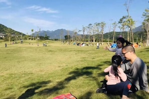 A grassy field with people sitting and walking, surrounded by trees and mountains in the background. - Bishui Xincun Yuese Villa (Guangzhou)