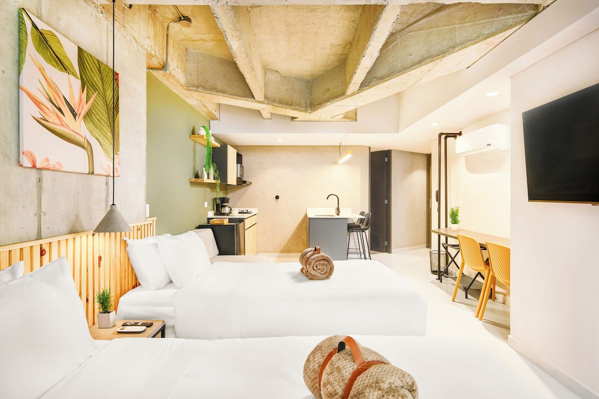 Una habitación de hotel moderna con una cama grande, un escritorio, una silla y una pequeña cocina.