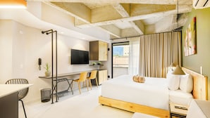 A modern hotel room with a large bed, a desk with chairs, a TV, and a view of the outdoors.
