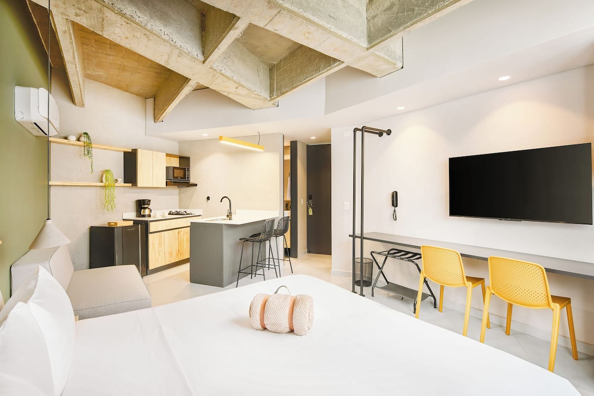 Una habitación de hotel moderna con cama, escritorio, silla, televisión y kitchenette.