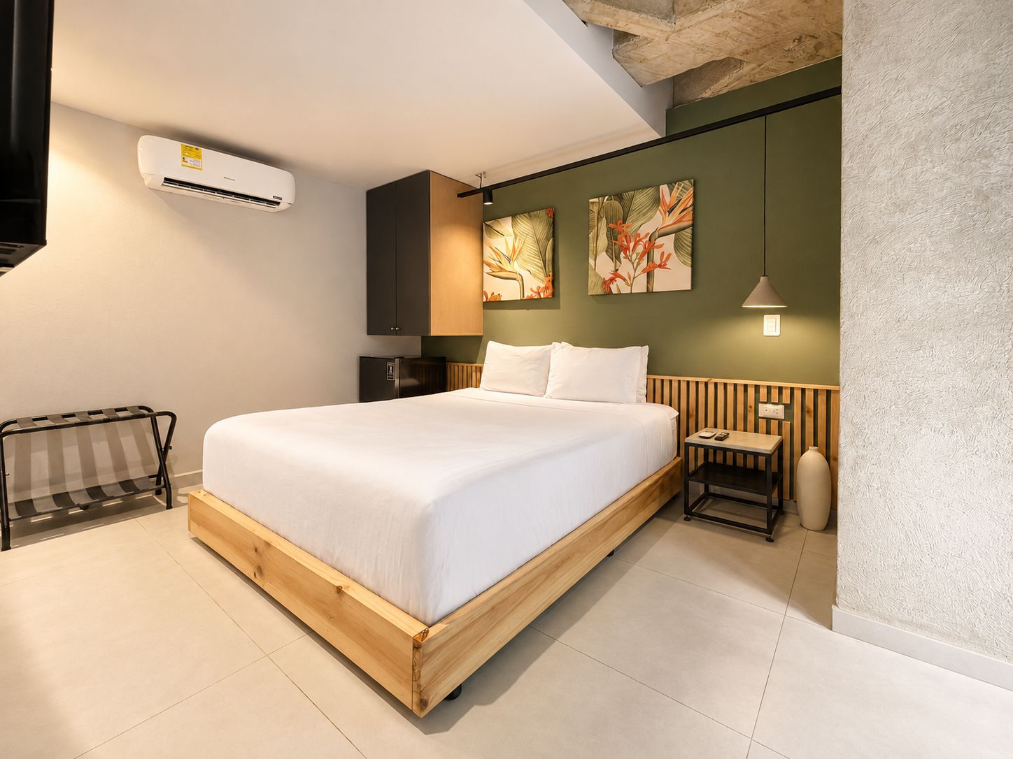 A modern bedroom with a wooden bed, a small bedside table, a nightstand, a wall-mounted air conditioner, and two wall art pieces.