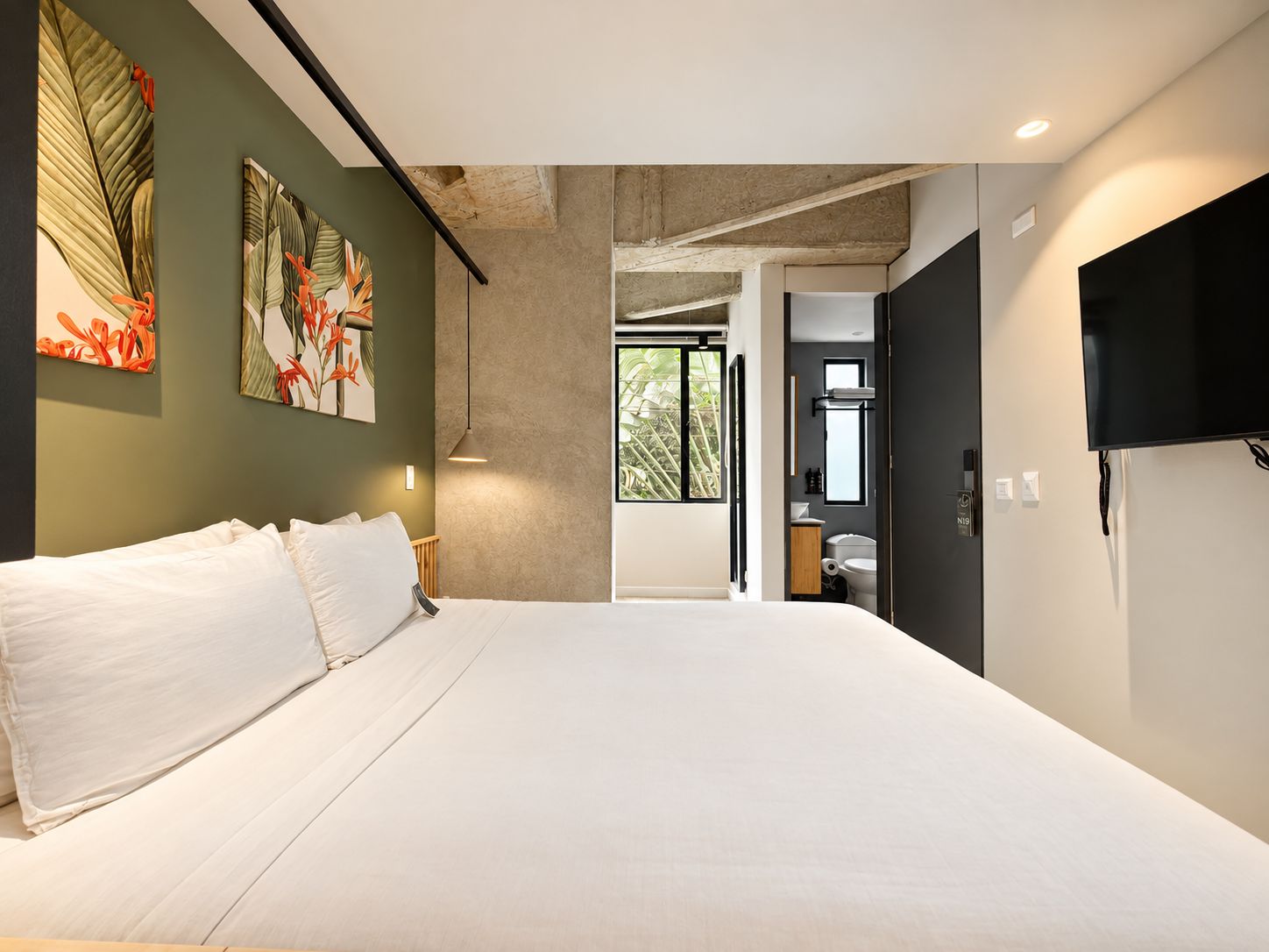 A modern bedroom with a large bed, a TV mounted on the wall, and a view into the bathroom.