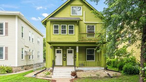 A two-story house with a green exterior, a front porch, and a small balcony. - Serenity suite 1-bedroom house, AC, WiFi, minutes from Minneapolis, pet friendly (Minneapolis)