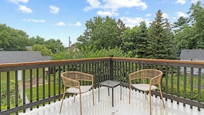 A wooden deck with two wicker chairs and a small table, surrounded by a wooden railing, overlooking a green landscape with trees and a house in the background. - Serenity suite 1-bedroom house, AC, WiFi, minutes from Minneapolis, pet friendly (Minneapolis)