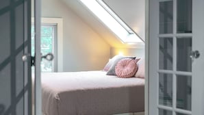 A bedroom with a sloped ceiling, a bed with pink bedding, a window with blinds, and a door with glass panels. - Serenity suite 1-bedroom house, AC, WiFi, minutes from Minneapolis, pet friendly (Minneapolis)