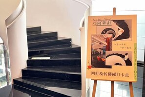 A staircase with a black marble finish and a poster on an easel with text and images. - Meridian Hotel (Chongqing)