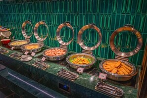 A buffet with various food items in metal containers, set against a green tiled wall. - Meridian Hotel (Chongqing)