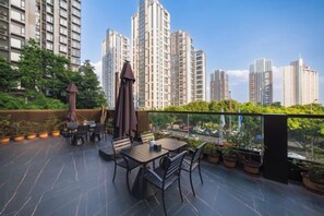 Una terraza exterior con mesas y sillas, plantas en macetas y vistas a edificios altos.