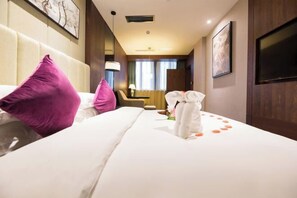 Habitación de hotel con una cama grande, dos almohadas, una mesita de noche, una lámpara y un televisor montado en la pared.