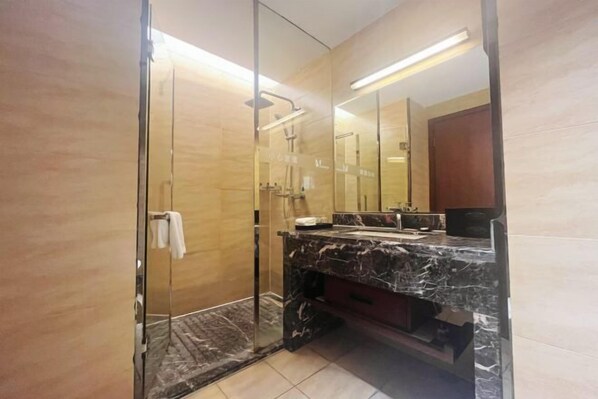 Un baño moderno con cabina de ducha de vidrio, tocador de mármol y un espejo grande.