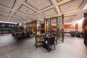 Un comedor moderno con mesas y sillas, una división de vidrio y vistas al exterior.