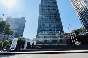 Un edificio alto con fachada de vidrio moderna, rodeado de otros rascacielos, y un cielo despejado arriba.