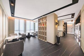 Un moderno vestíbulo de hotel con una zona de estar, una estantería y una recepción.