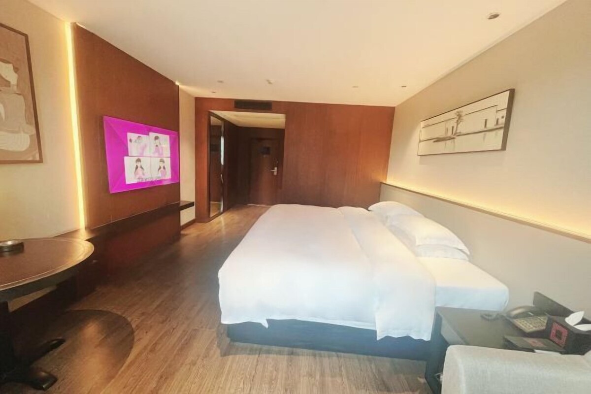 Habitación de hotel con una cama grande, un escritorio y una silla. Hay una puerta que da a otra habitación y una obra de arte colgada en la pared.