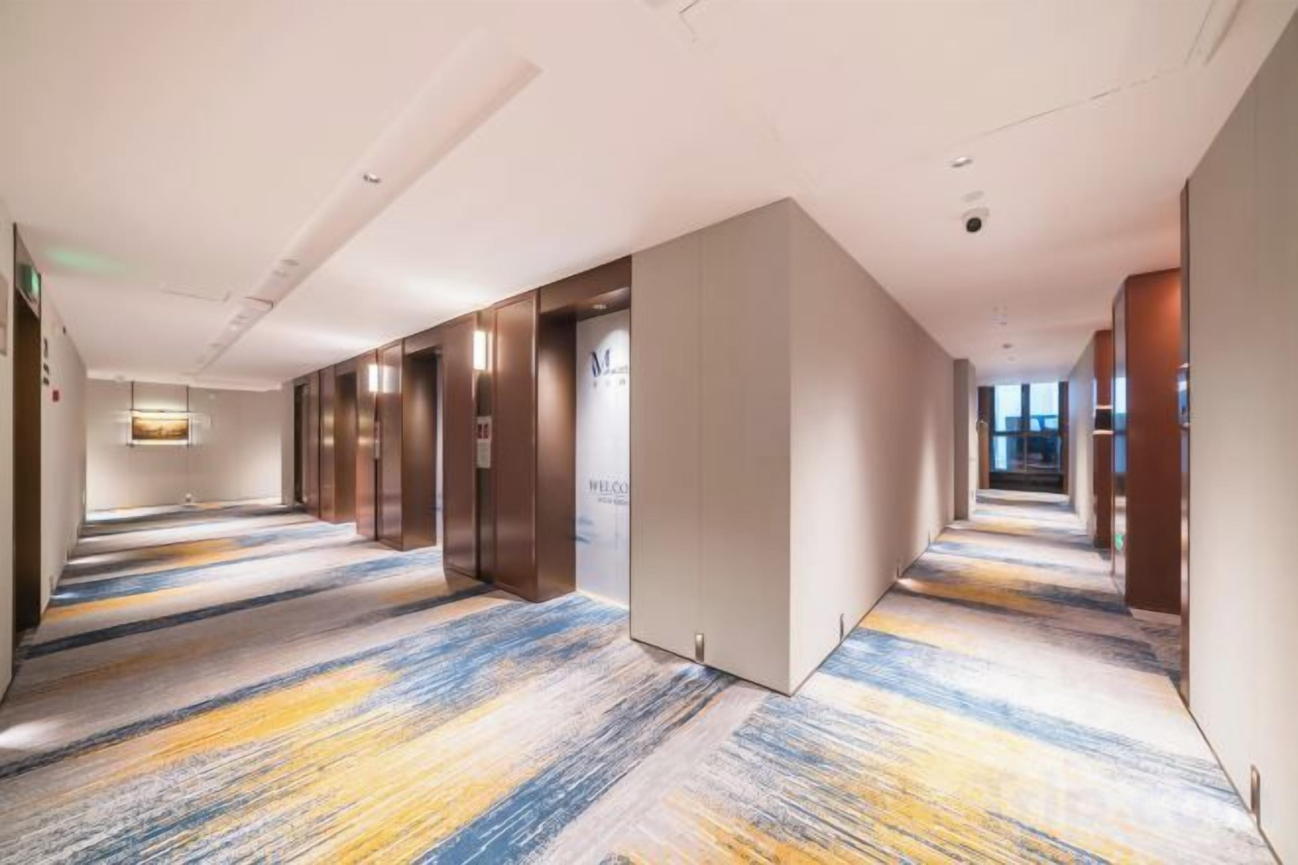 Corredor de hotel com carpete estampado, portas de elevador e área de recepção.
