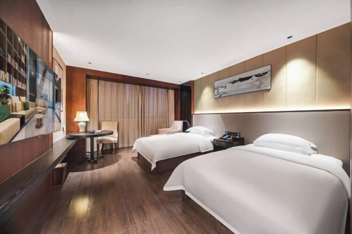 A hotel room with two beds, a desk with a chair, a lamp, and a painting on the wall.
