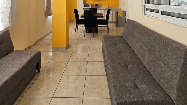 Una sala de estar con ventilador de techo, un comedor con mesa y sillas, y una cocina al fondo.