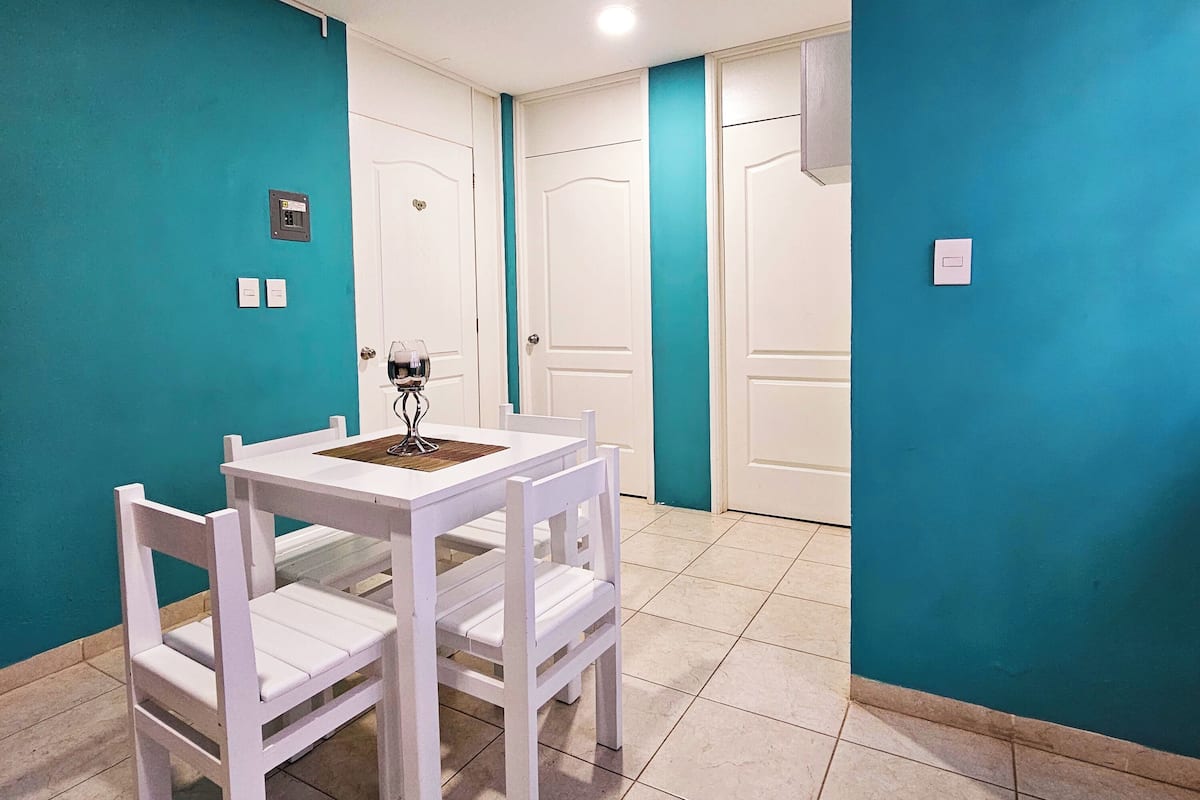A small dining area with a white table and chairs, a wine glass, and a wall-mounted light fixture.