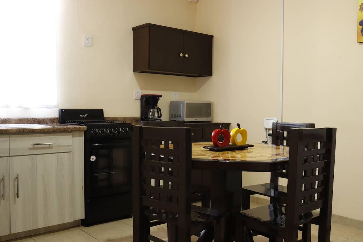 A kitchen with a stove, microwave, and cabinets. There are two chairs and a table with apples on it.