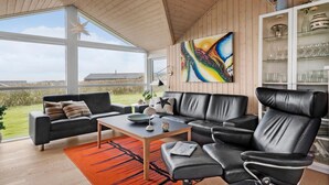 A modern living room with a black leather sofa, a wooden coffee table, and a colorful abstract painting on the wall. - Cozy home in Lemvig with sauna (Lemvig)