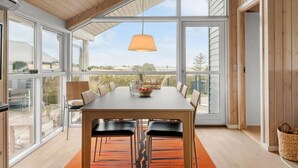A spacious dining area with a large table and chairs, large windows offering a view of the outdoors, and a hanging light fixture. - Cozy home in Lemvig with sauna (Lemvig)