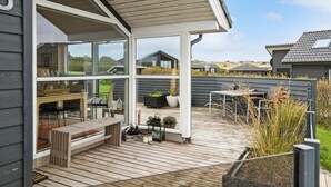 A covered outdoor patio with a wooden deck, seating area, and potted plants. - Cozy home in Lemvig with sauna (Lemvig)