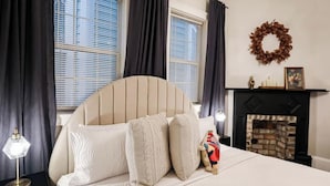 Una camera da letto con un letto, tende scure, un camino e una ghirlanda appesa al muro.