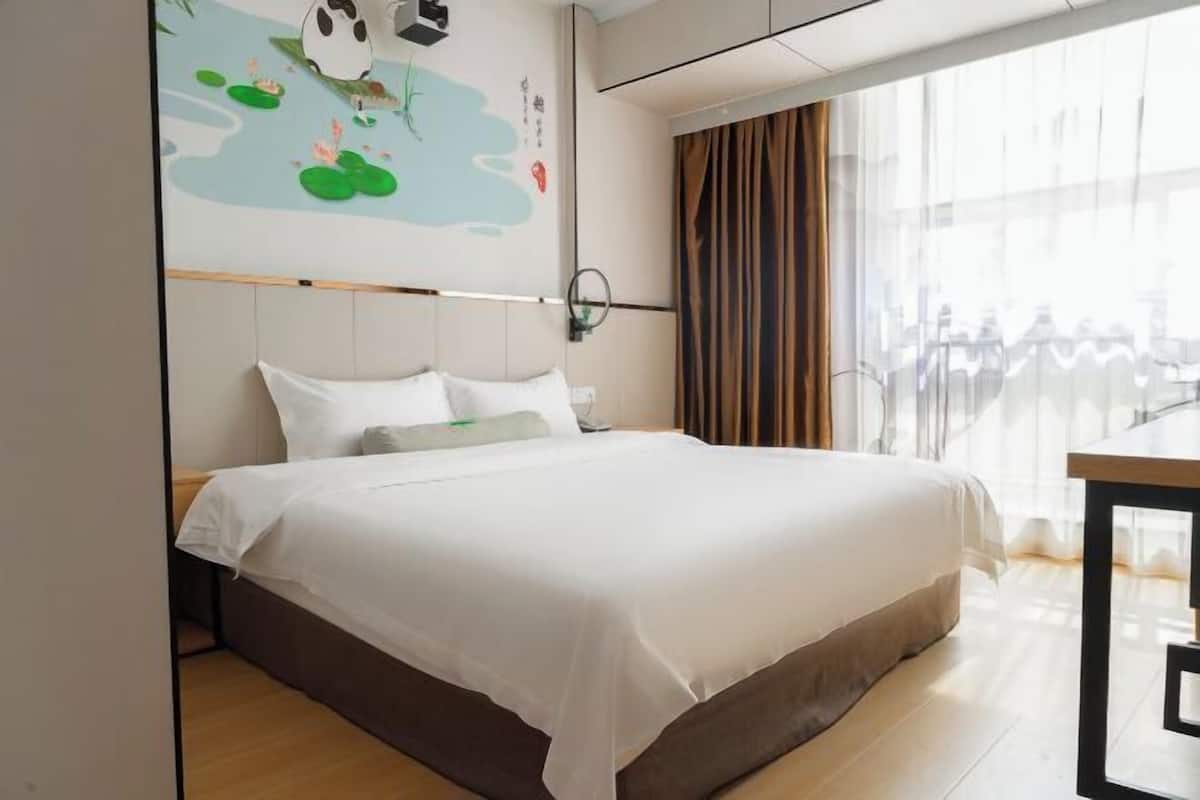 Habitación de hotel con una cama grande, vista a la ciudad y un mural de panda en la pared.
