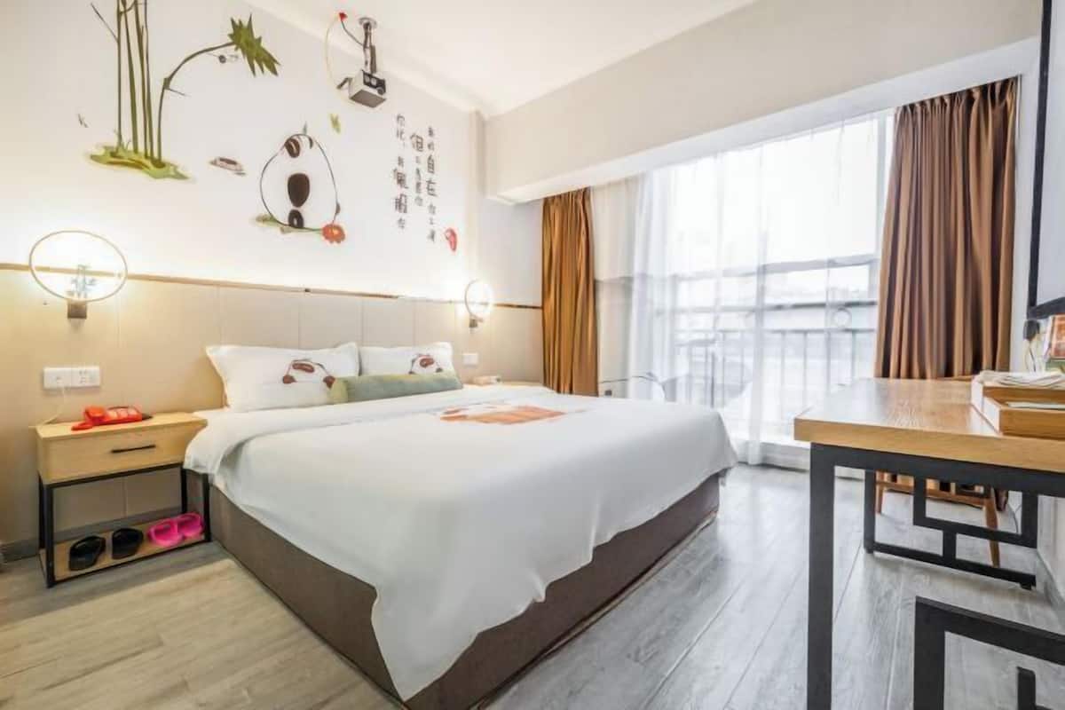 Habitación de hotel con cama, mesita de noche y vistas al exterior.