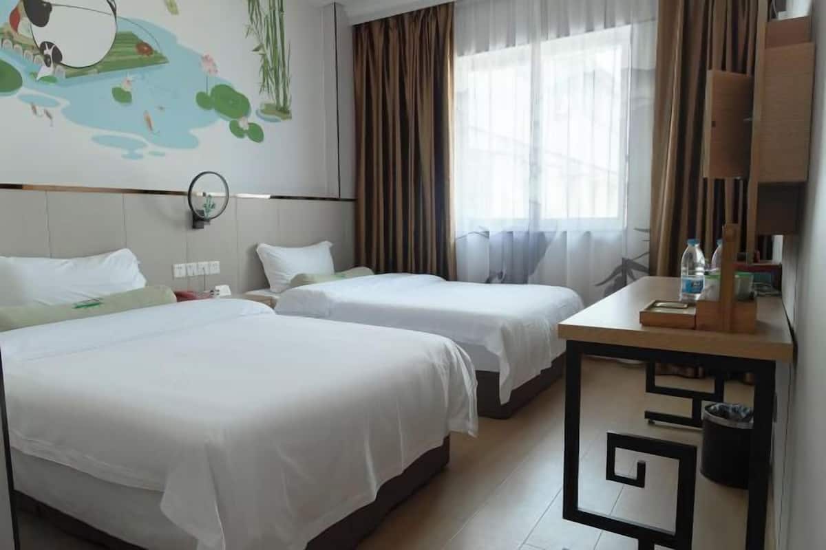 Una habitación de hotel con dos camas individuales, un escritorio con silla, un espejo y un mural en la pared.