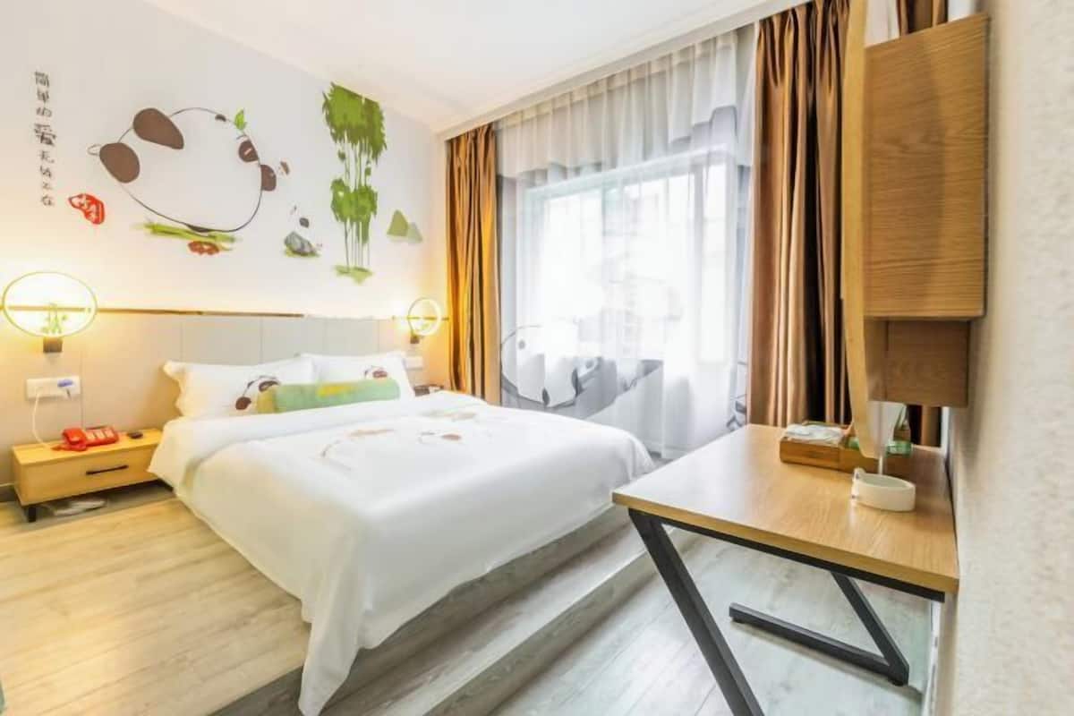 Una habitación de hotel con cama, mesita de noche, lámpara y ventana con cortinas.