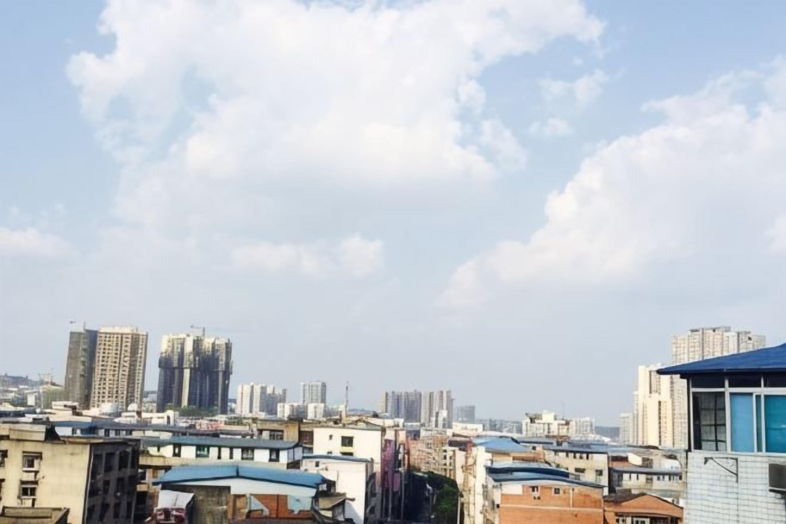 Ένα αστικό τοπίο με πολλά κτίρια, μερικά από τα οποία έχουν μπλε στέγες, κάτω από έναν ουρανό με διάσπαρτα σύννεφα.