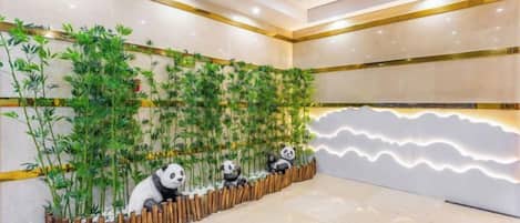 A reception area with a bamboo wall, a row of panda statues, and a modern light design on the wall.
