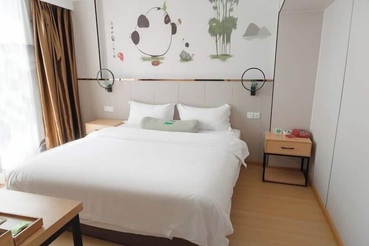 Habitación de hotel con cama, mesita de noche, una obra de arte en la pared y ventana con cortinas.