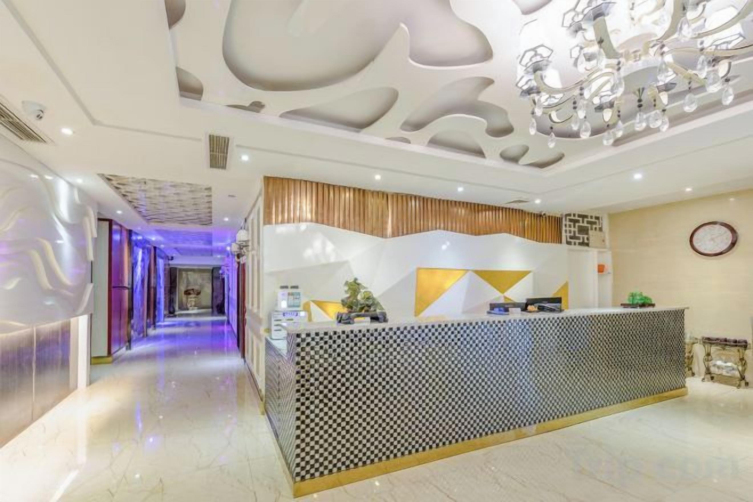 A hotel reception area with a modern design, featuring a reception desk, a clock on the wall, and a hallway leading to other rooms.