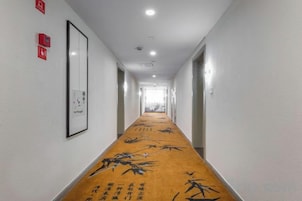 Un pasillo de hotel con piso alfombrado, obras de arte enmarcadas en las paredes y puertas que dan a las habitaciones.