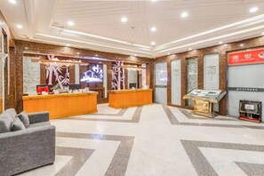 Zona de recepción de hotel con mostrador, un espacio de descanso con sofá y una vitrina.