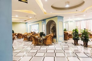 Un comedor de hotel con mesas y sillas redondas, piso de baldosas y una pared azul decorativa.