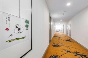 Een gang met een tapijt met bamboepatronen, witte muren en aan de linkerzijde kunstwerken in lijsten.